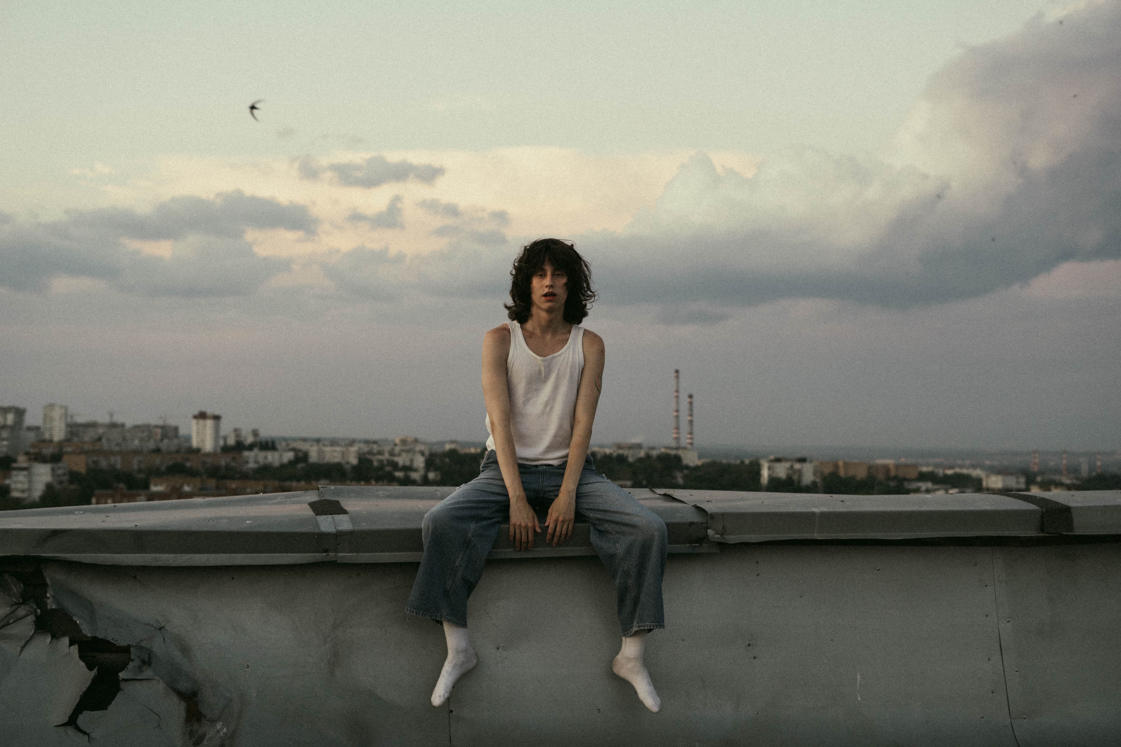 Woman sitting on a rooftop ledge above the city under a cloudy sky