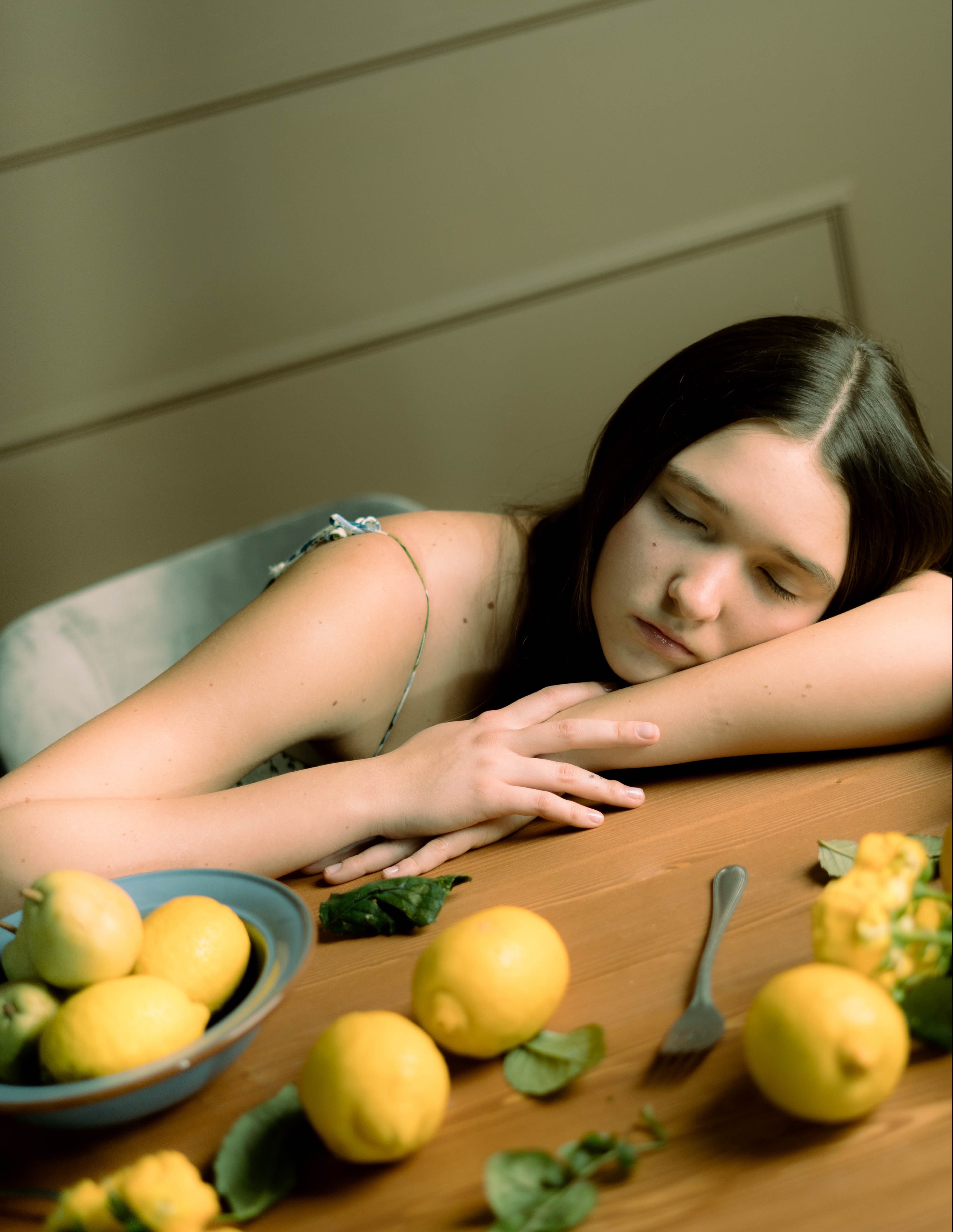 Woman resting her head on a table beside a bowl of lemons