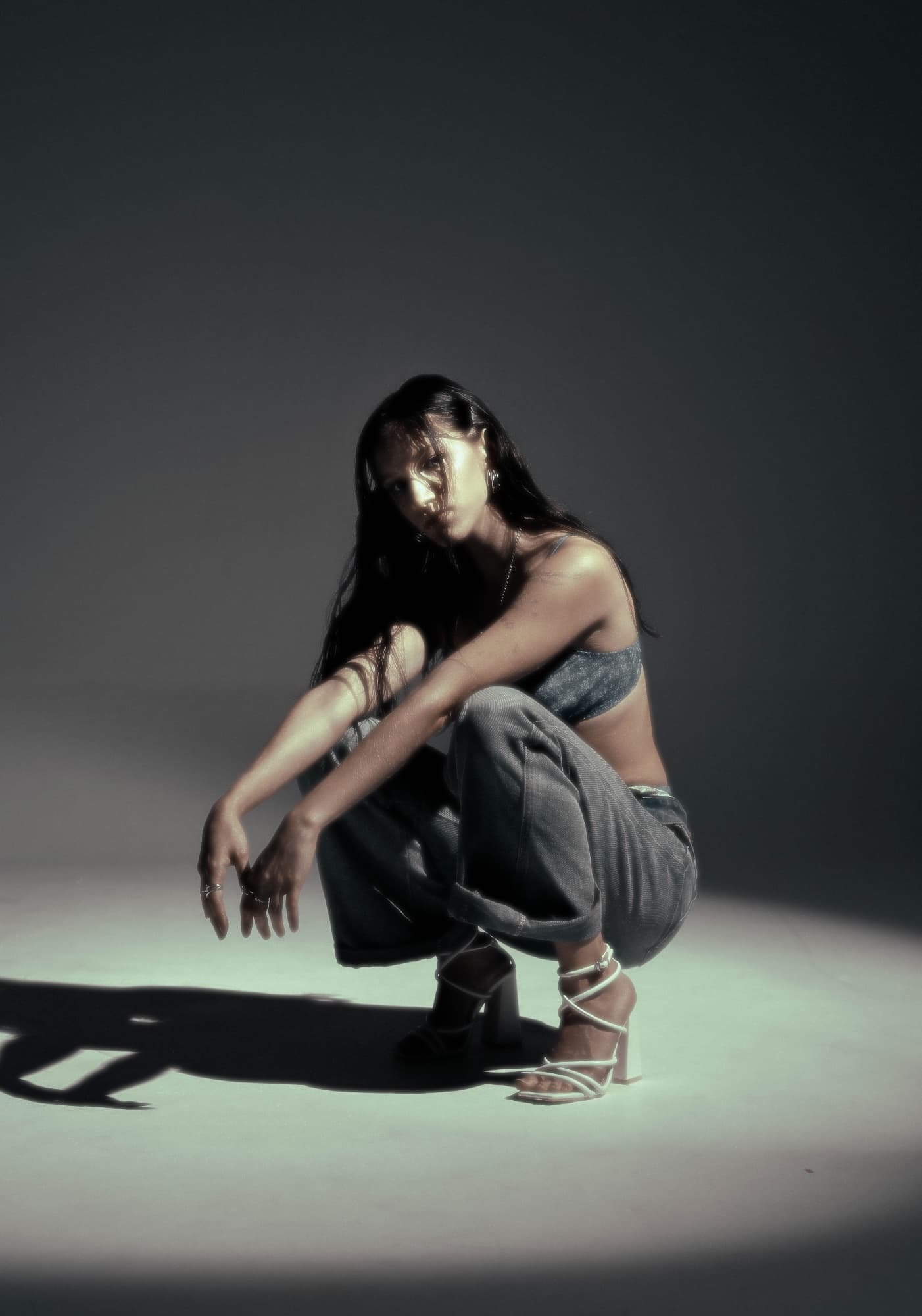 Woman crouching in a pool of light in a dark studio