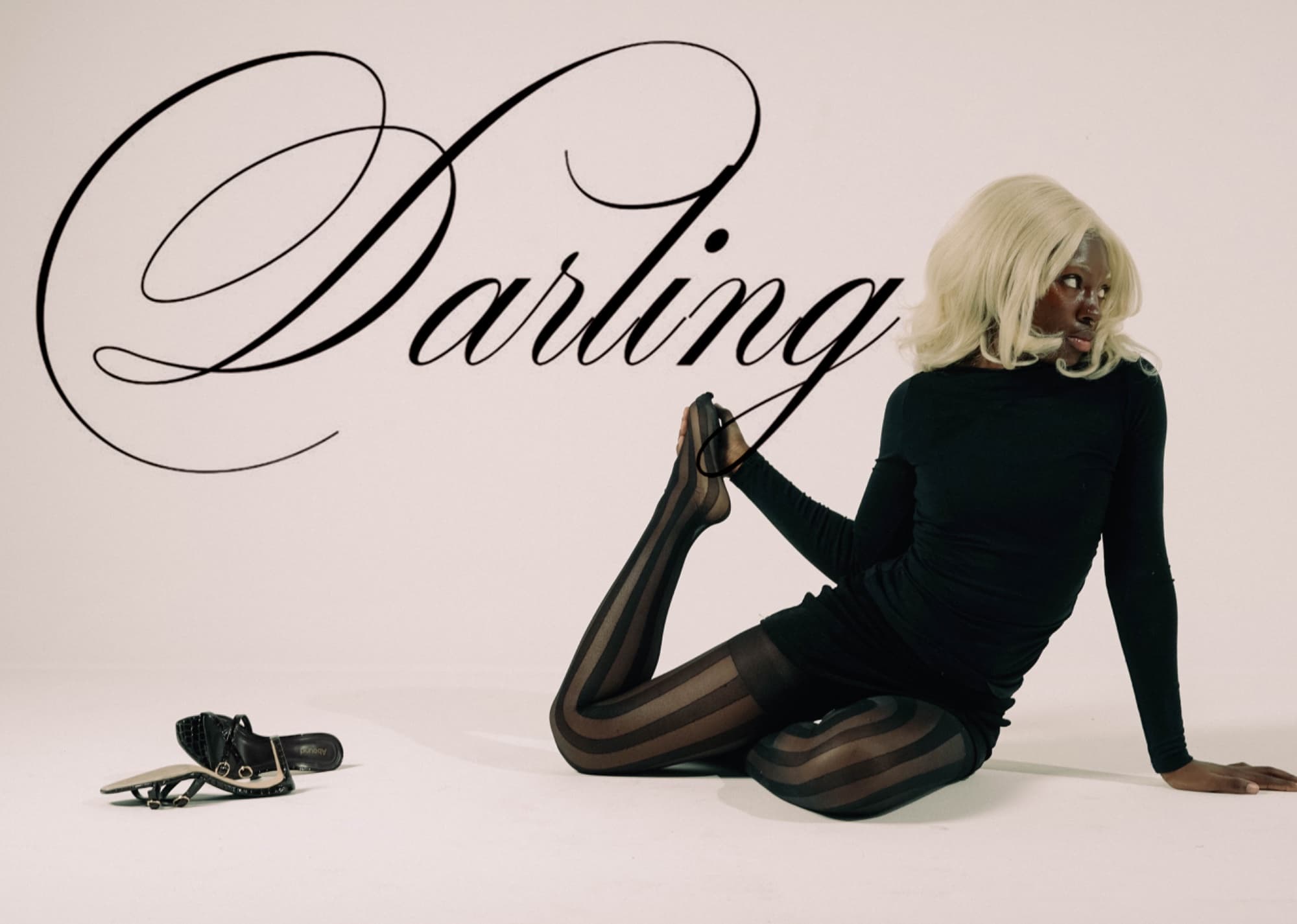 Model in black seated on a beige set beside the word Darling in script