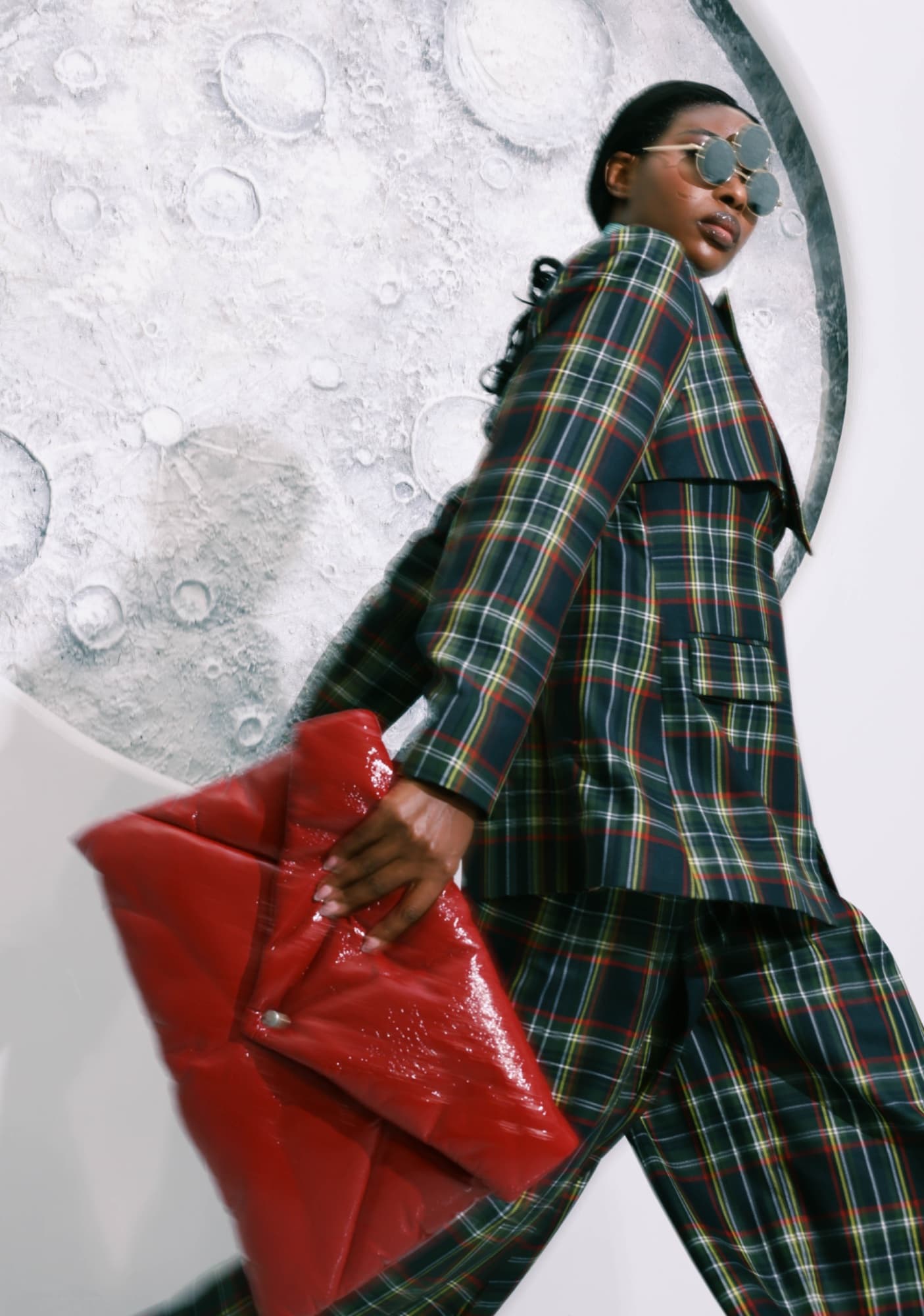 Model in a plaid suit striding with a red leather bag