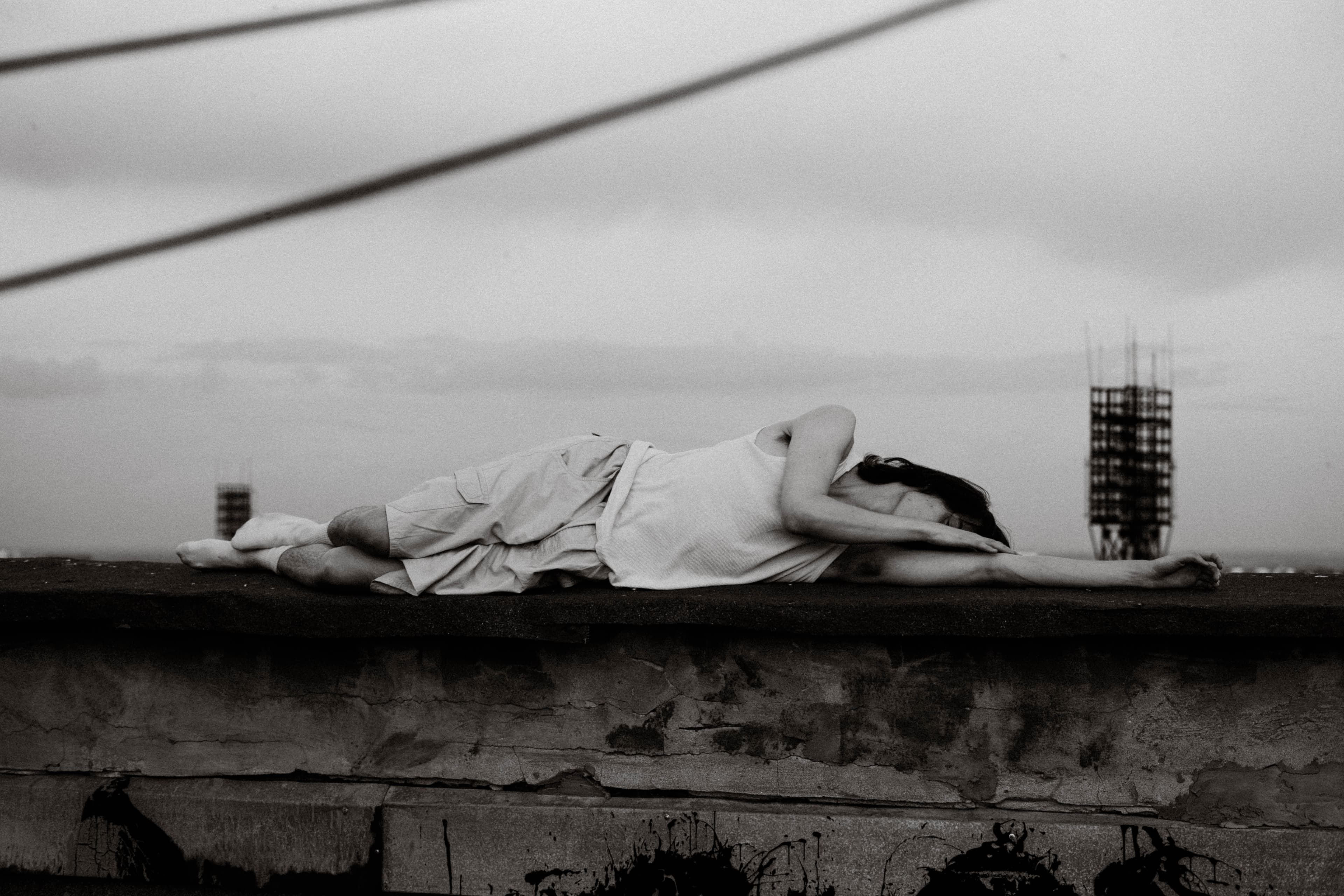 Woman lying on a rooftop ledge under a grey sky